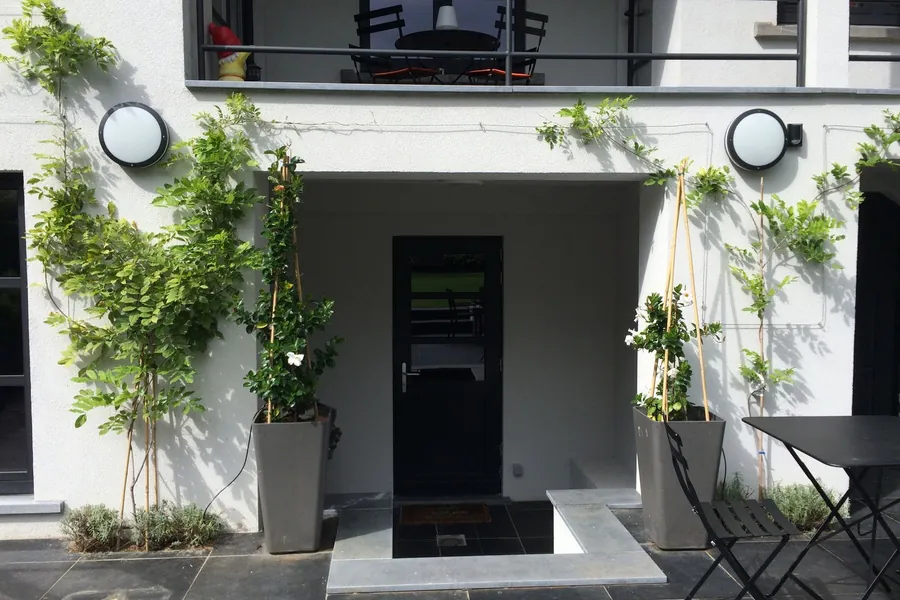 Tuin met witte gevel, klimplanten in plantenbakken en een terras met bistrostoelen