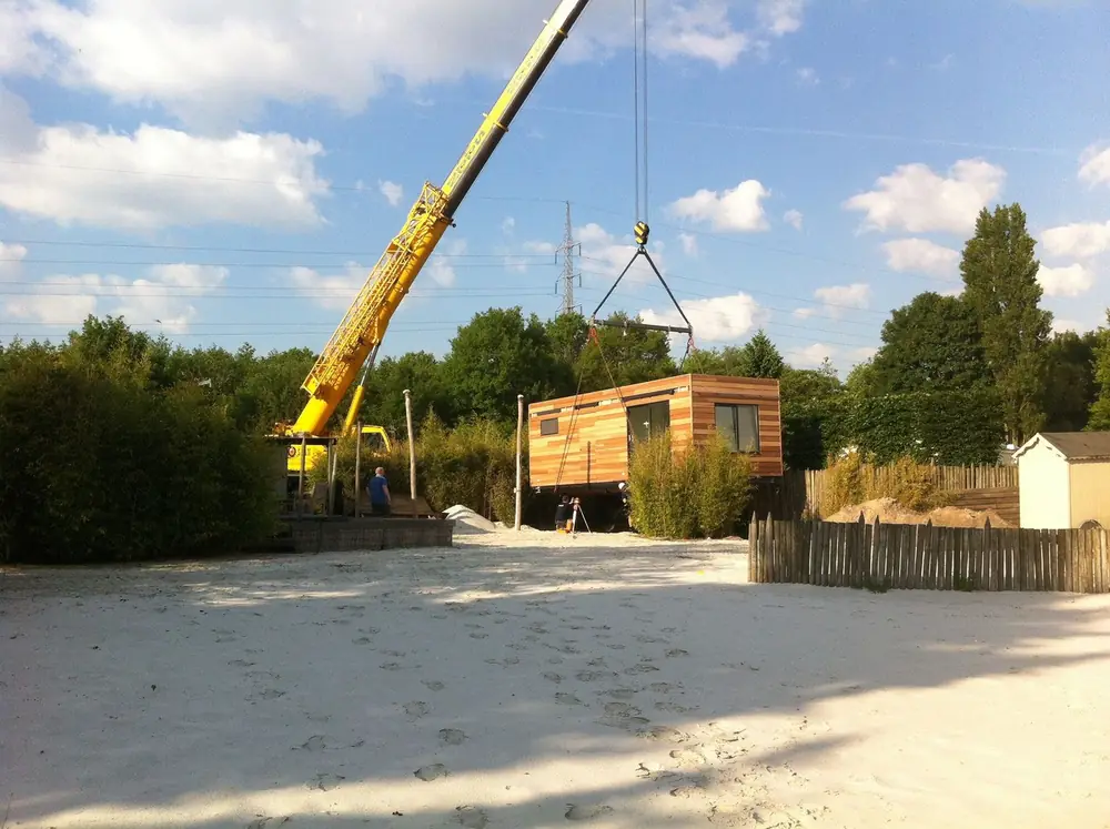 Kraan zet een houten tuinhuis op zijn plek naast het zand van de beachtuin