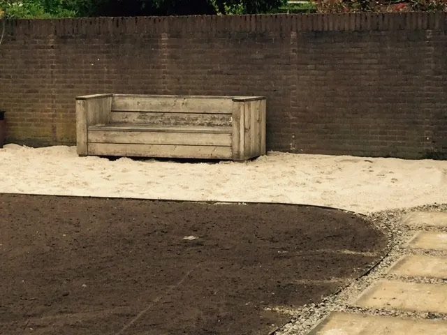 Betonnen zitbank op het zand tegen een bakstenen muur