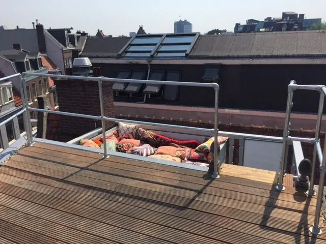 Dakterras met houten vlonder en kussens, uitkijkend over de daken van Amsterdam